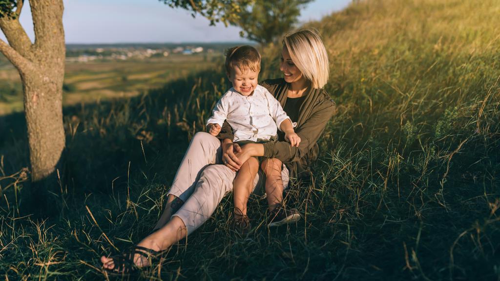 feliz jovem mãe e bonito pequeno filho sentado juntos na grama verde ao pôr do sol
 - Foto, Imagem