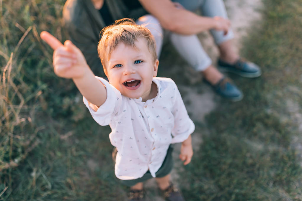 vista de ángulo alto de adorable niño feliz apuntando con el dedo y sonriendo a la cámara al aire libre
 - Foto, Imagen
