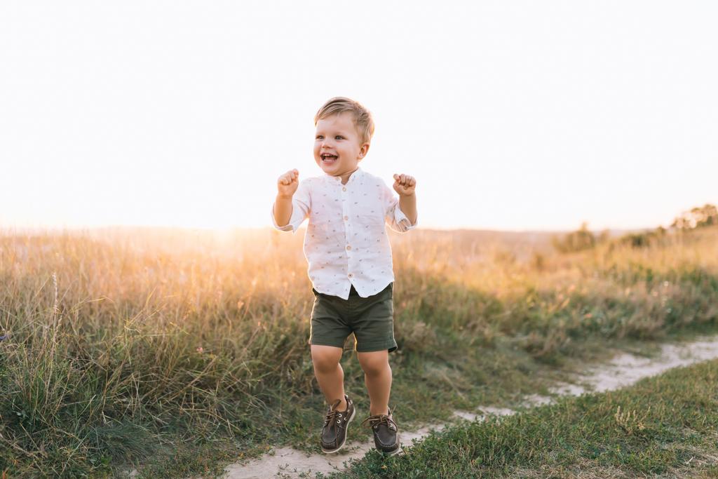 Urocza szczęśliwy chłopiec chodzenie na wiejskiej drodze o zachodzie słońca  - Zdjęcie, obraz
