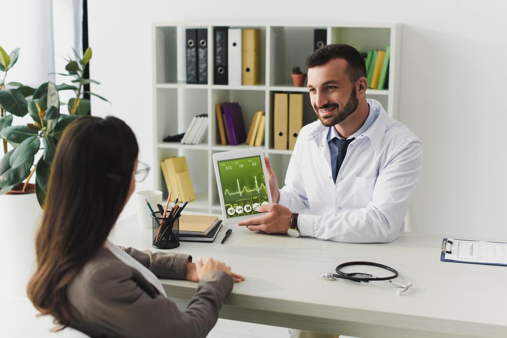 usmívající se doktor ukazuje pacienta miniaplikace s pulzní zařízení v klinice - Fotografie, Obrázek