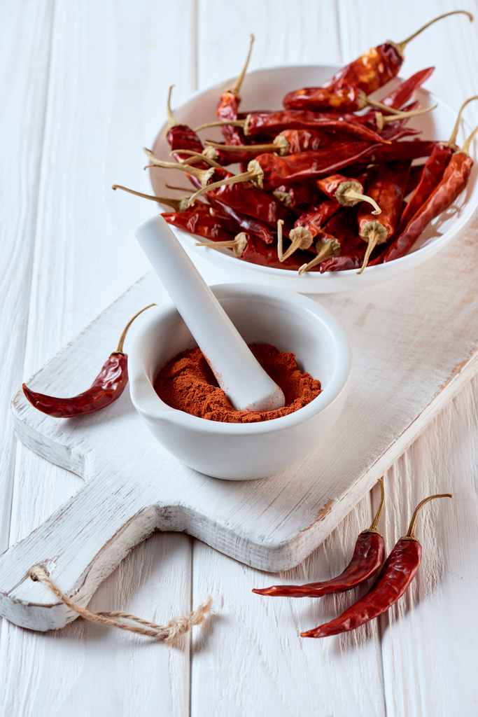close up view of grinded chili pepper in mortar with pestle on white wooden surface - Photo, Image