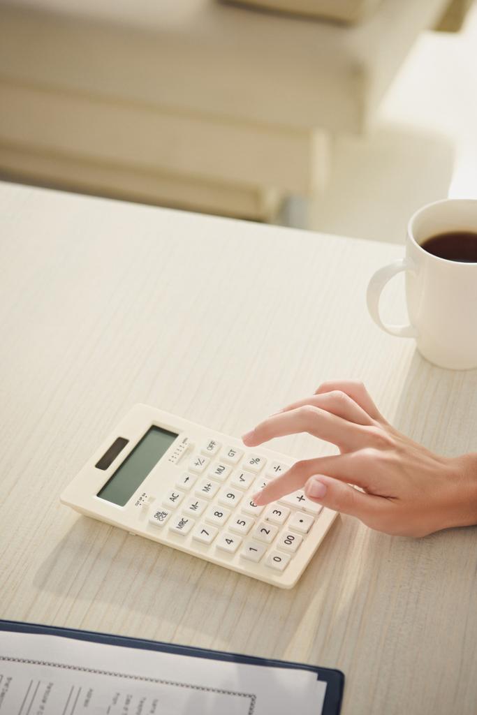 vue recadrée de femme comptant finances sur calculatrice à table avec tasse de café
 - Photo, image