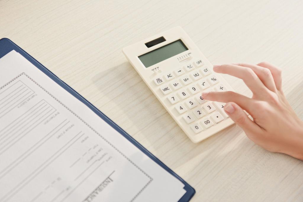 обрізаний вид жінки, що рахує фінанси на калькуляторі за столом з формою страхової вимоги
 - Фото, зображення