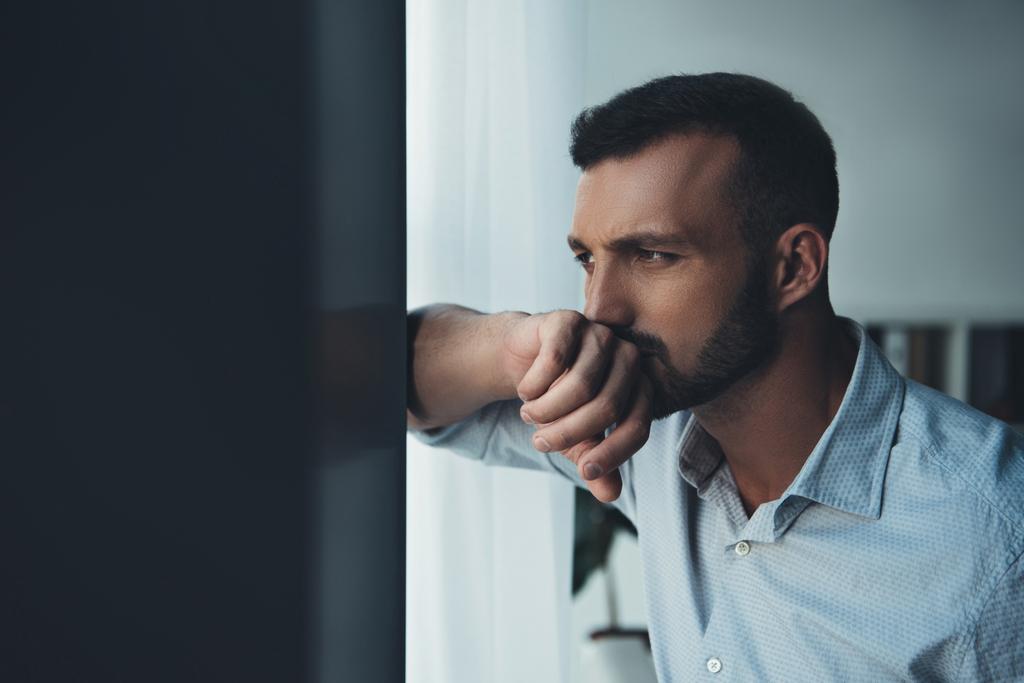 расстроенный задумчивый мужчина смотрит в окно на дом
 - Фото, изображение