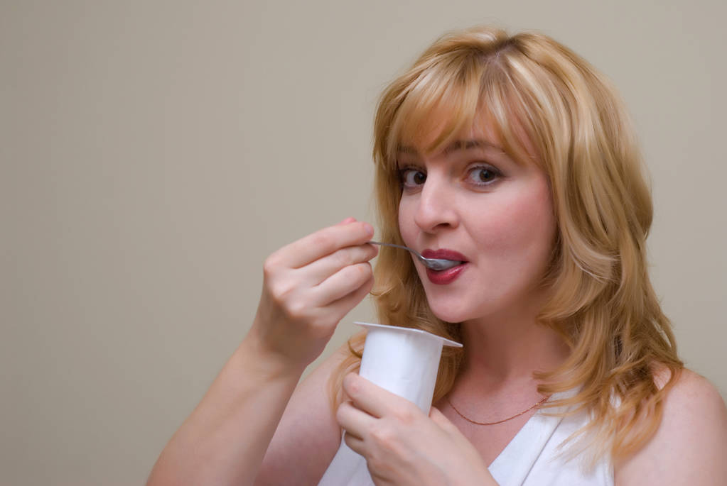 hermosa mujer rubia sonriendo comiendo yogur posando sobre fondo beige estudio
 - Foto, imagen
