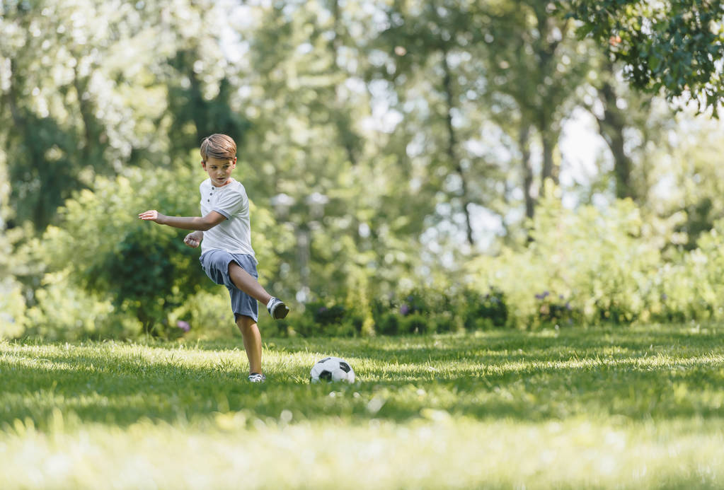 vista a tutta lunghezza del ragazzo felice che gioca con il pallone da calcio sull'erba nel parco
 - Foto, immagini