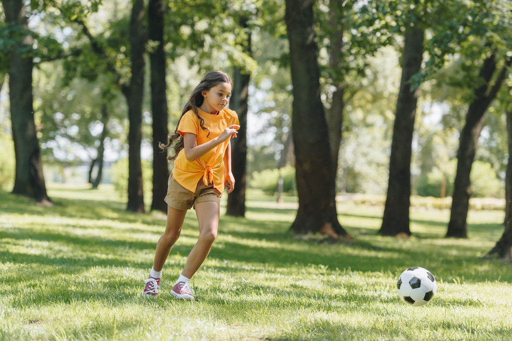 Προβολή πλήρους μήκους όμορφο παιδί τρέχει στο χορτάρι και τοποθέτηση με μπάλα στο πάρκο - Φωτογραφία, εικόνα