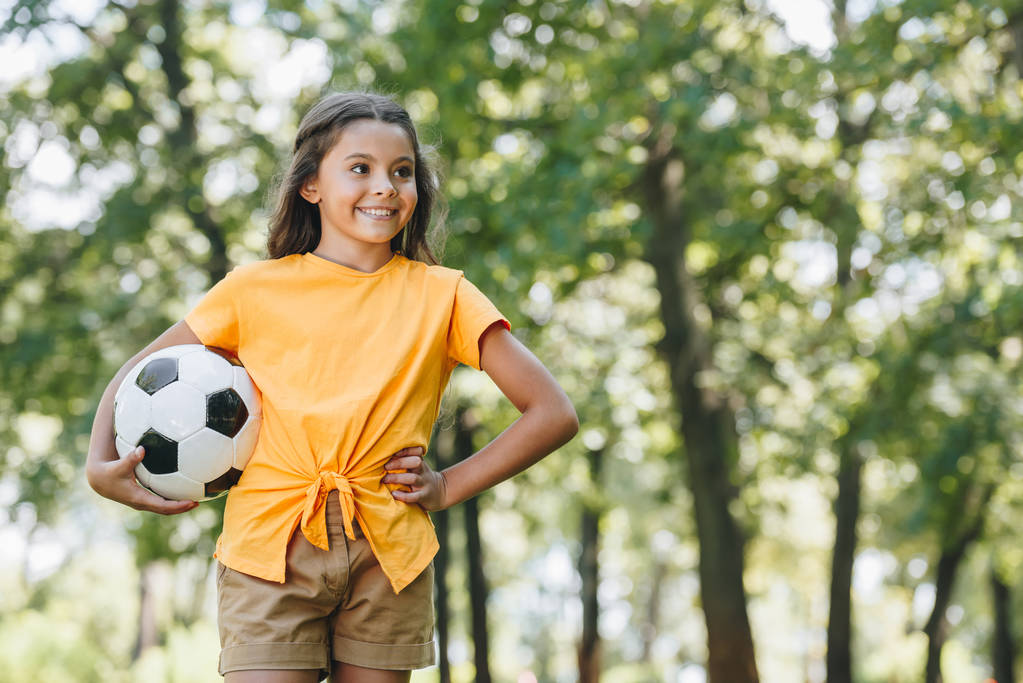 criança feliz bonito segurando bola de futebol e olhando para longe no parque
 - Foto, Imagem