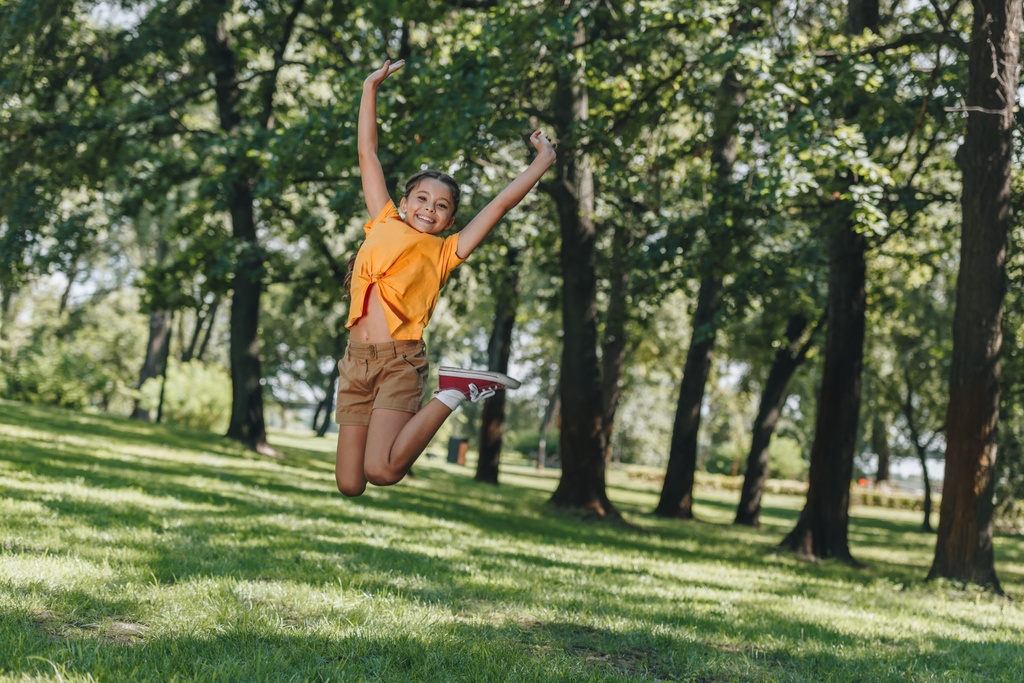söpö iloinen lapsi hyppää ja hymyilee kameralle puistossa
  - Valokuva, kuva