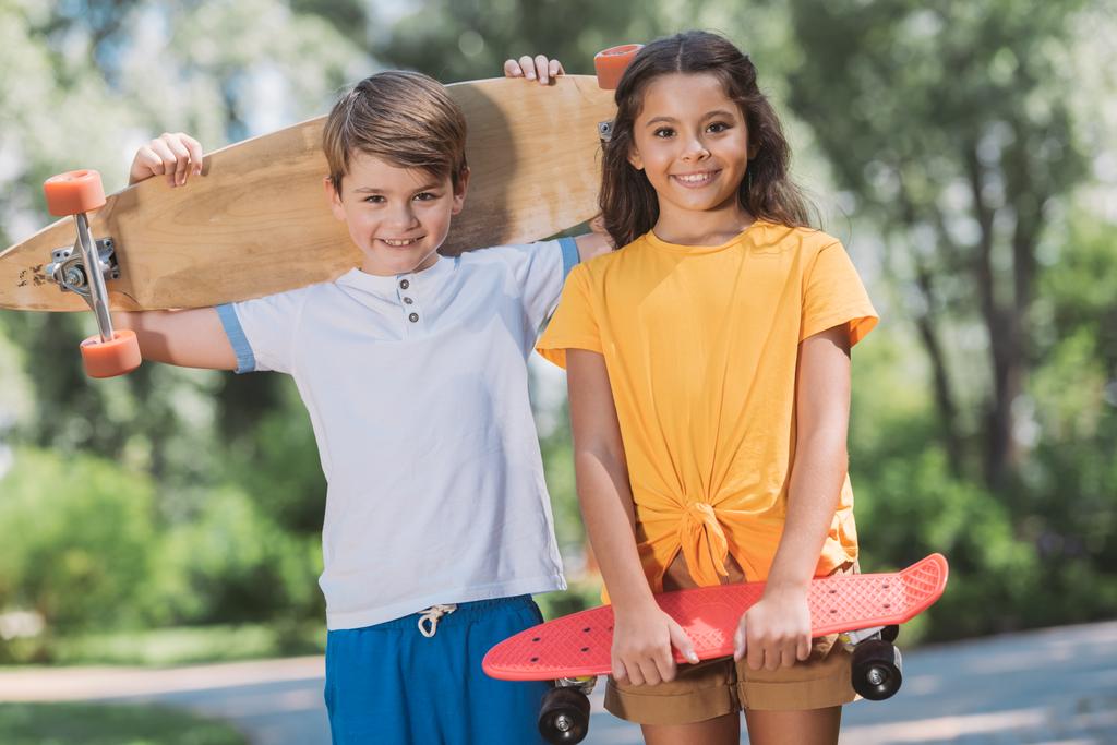 симпатичные счастливые дети, держащие в руках скейтборды и улыбающиеся камерам в парке
 - Фото, изображение