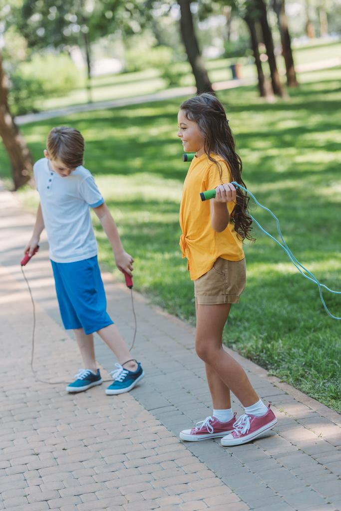 Urocza szczęśliwe dzieci bawiąc się przeskakując liny w parku  - Zdjęcie, obraz
