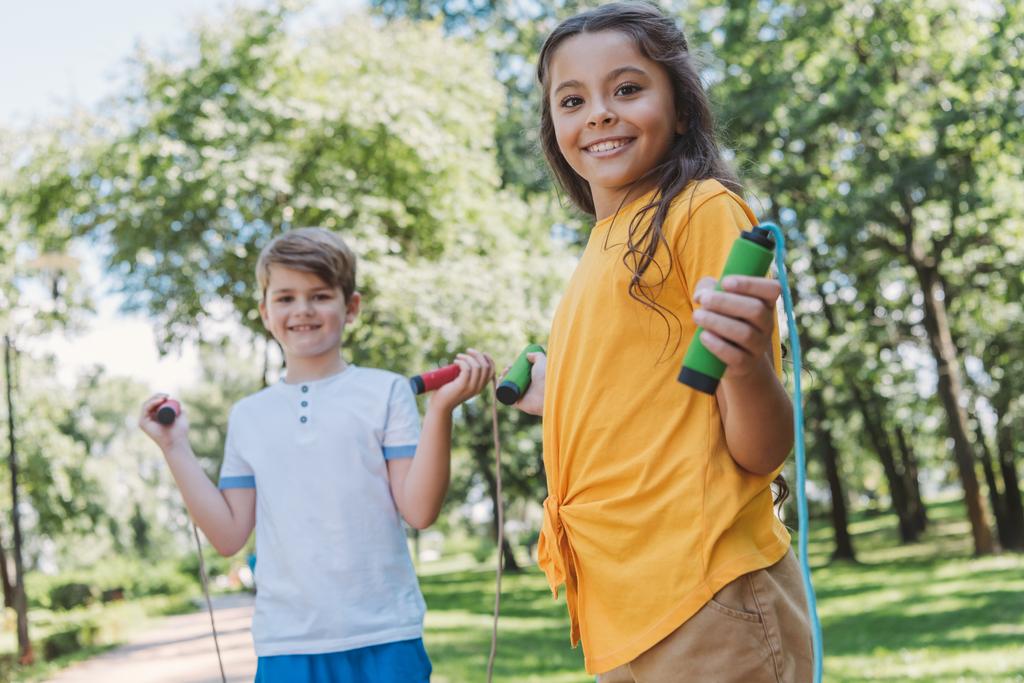 αξιολάτρευτο ευτυχής παιδιά πεζοπορία παρακάμπτοντας τα σχοινιά και να χαμογελά στη φωτογραφική μηχανή στο πάρκο - Φωτογραφία, εικόνα