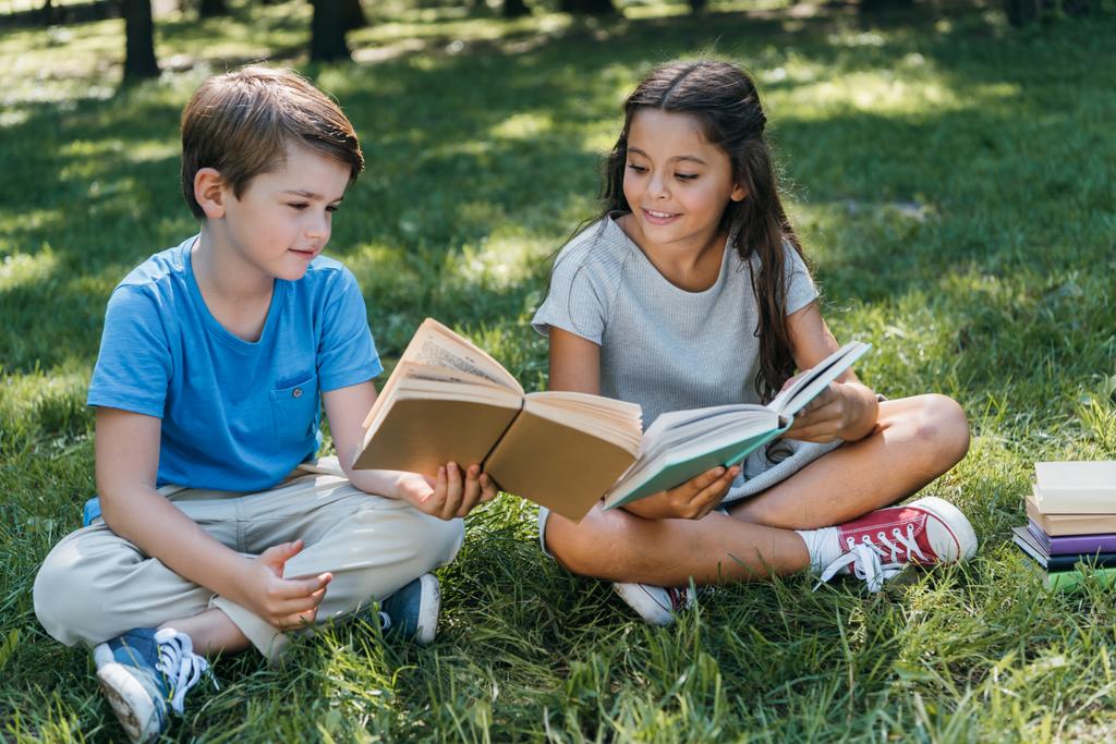 милые маленькие дети сидят на траве и читают книги
 - Фото, изображение