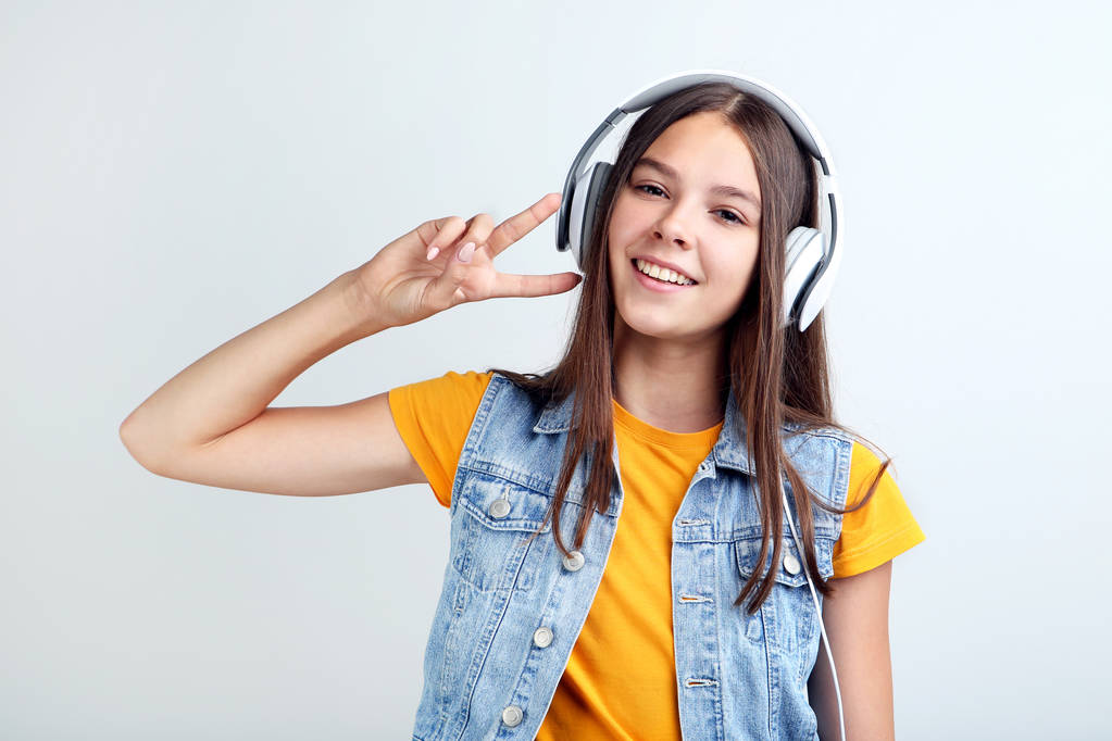 Jong meisje met koptelefoon op grijze achtergrond - Foto, afbeelding