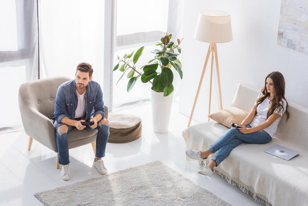 vista de ángulo alto de la pareja joven concentrada jugando videojuego con joysticks en casa
  - Foto, imagen