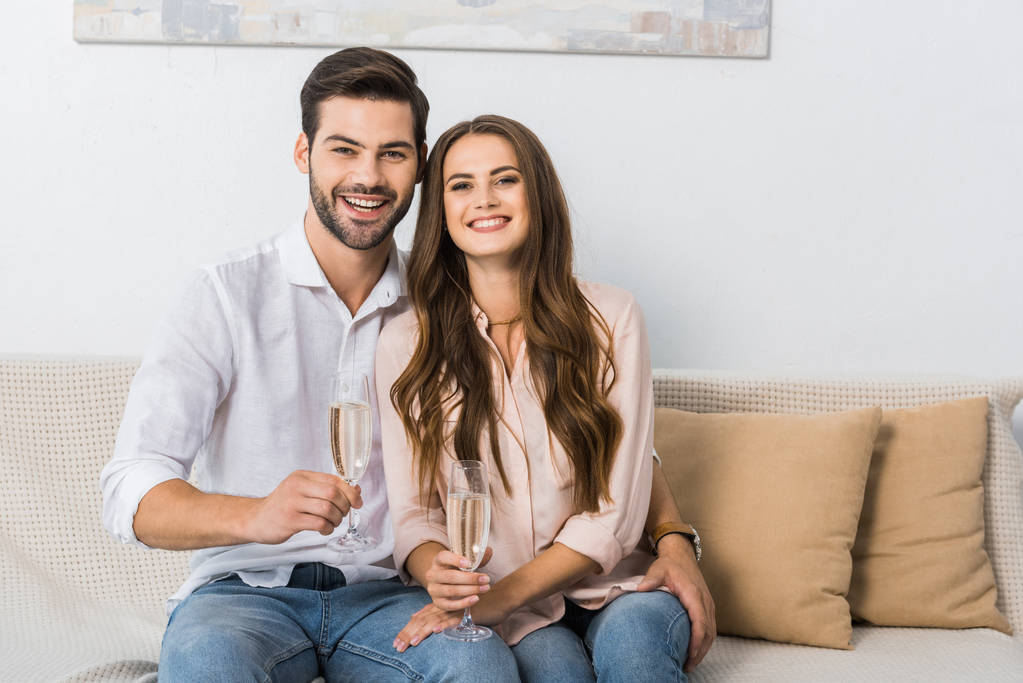 portrét šťastný mladý pár s sklenice šampaňského na gauči doma - Fotografie, Obrázek