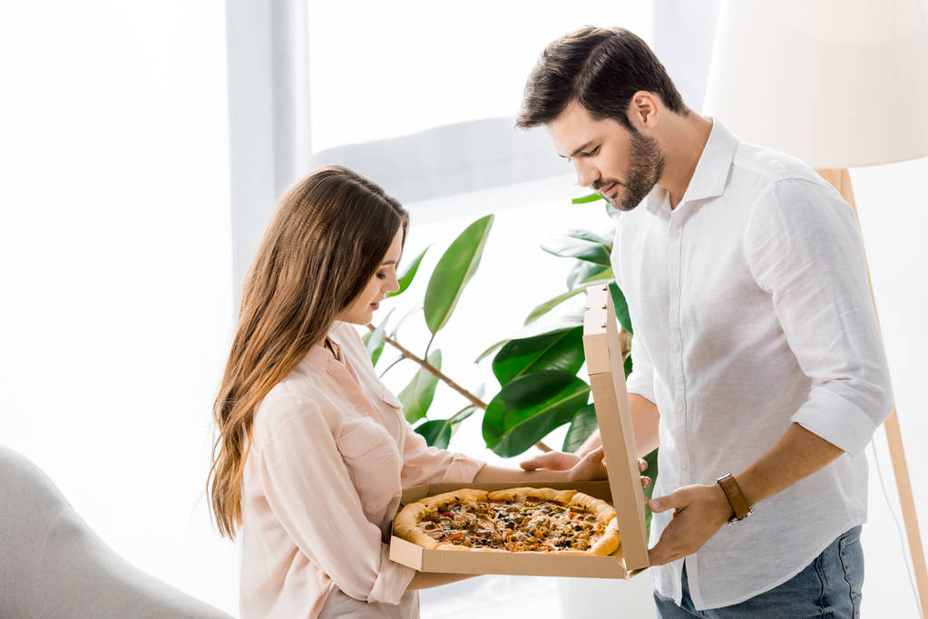 Widok z boku z młoda para ogląda z delivired pizza w papier pole w domu - Zdjęcie, obraz