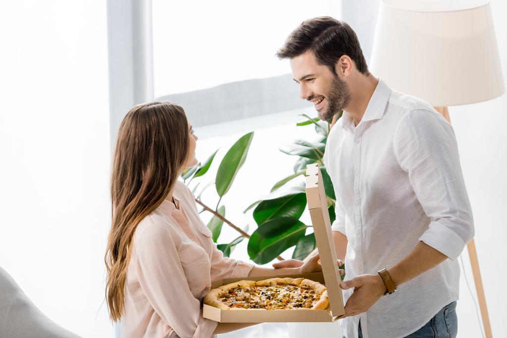 вид сбоку молодая пара с доставкой пиццы в бумажной коробке дома
 - Фото, изображение