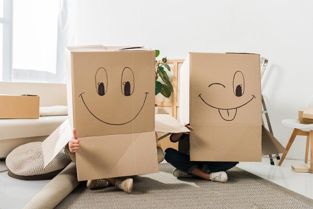 vue obscure du couple avec des boîtes en carton sur les têtes assises sur le sol à la nouvelle maison, déménagement concept de maison
 - Photo, image