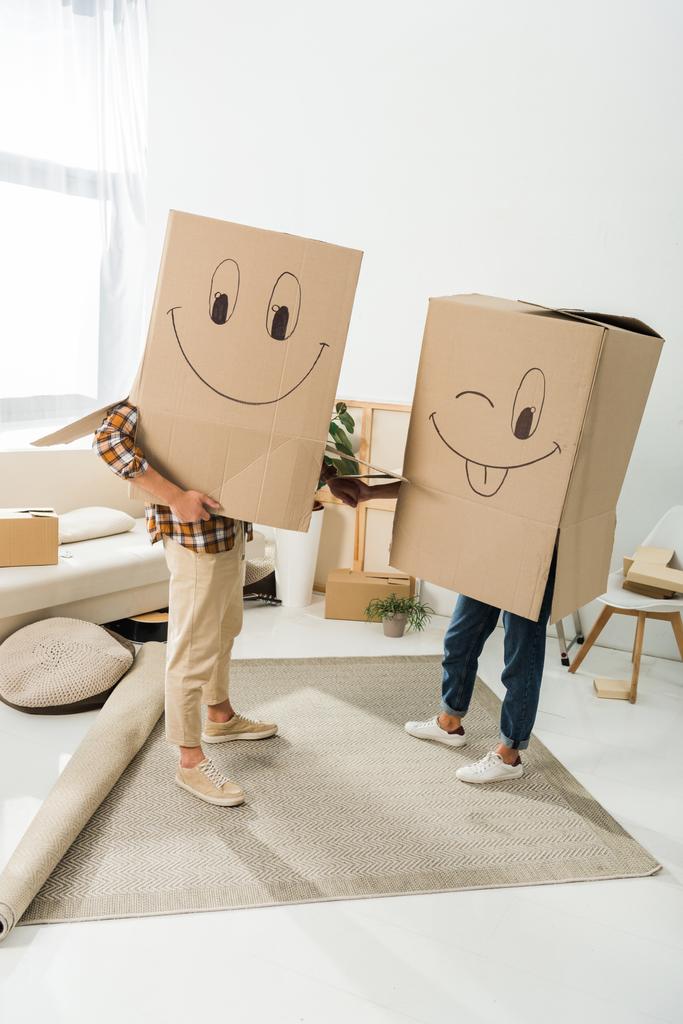 κρυμμένη άποψη του ζεύγους με τα κουτιά από χαρτόνι για κεφαλές, κρατώντας τα χέρια στο νέο σπίτι, κινείται home concept - Φωτογραφία, εικόνα