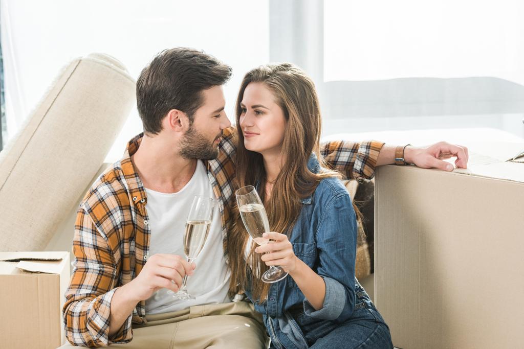 portrait of couple in love clinking glasses of champagne at new house with cardboard boxes, moving home concept - Photo, Image