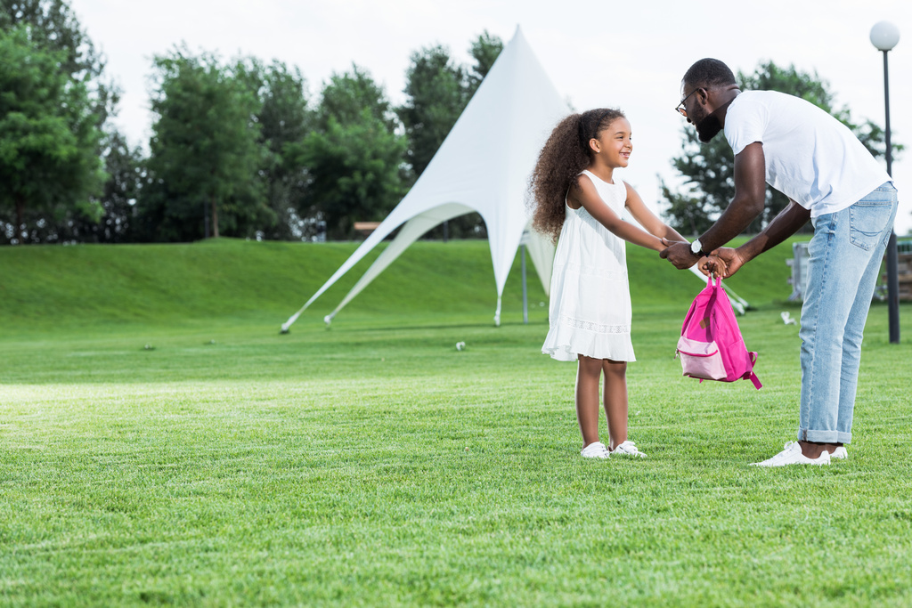 afro-americana filha dando saco escolar para o pai no parque
 - Foto, Imagem
