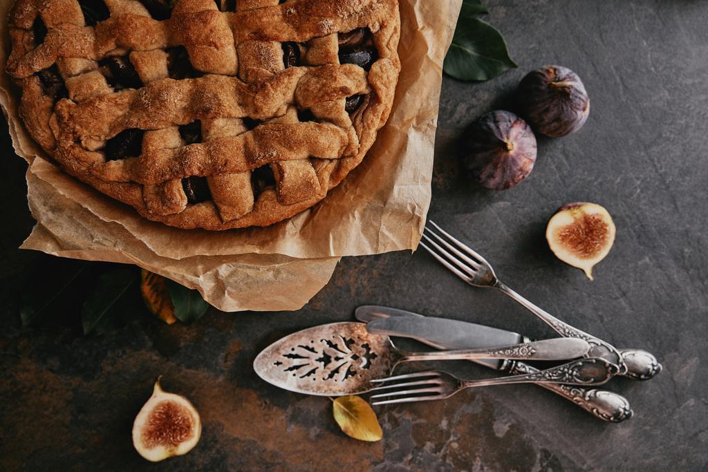 flat lay with homemade pie on baking paper, antique cutlery and fresh figs on dark tabletop - Photo, Image