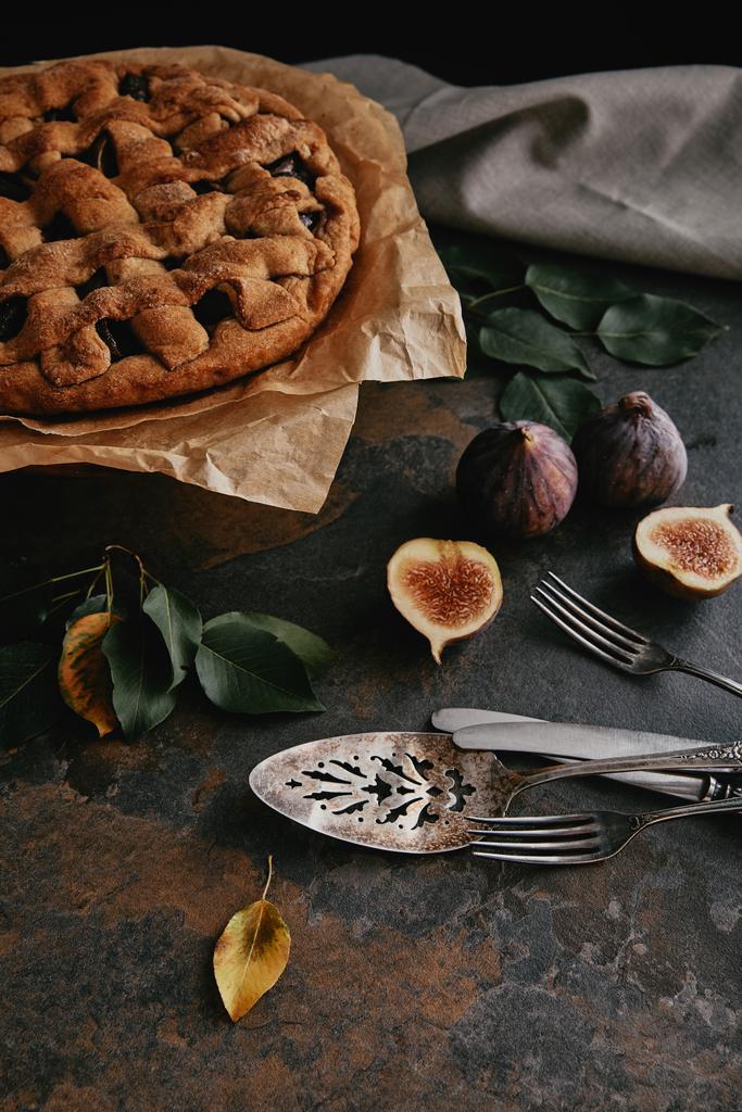 close up view of homemade pie on baking paper, antique cutlery and fresh figs on dark tabletop - Photo, Image