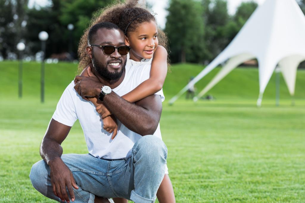 Африканская американская дочь обнимает отца в парке, и они отворачиваются.
 - Фото, изображение