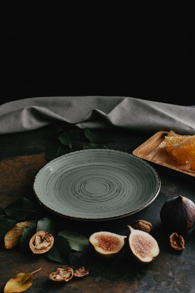 крупним планом вид на порожню тарілку, лісові горіхи, мед та інжир, розташовані на гранжевому столі з чорним тлом
 - Фото, зображення