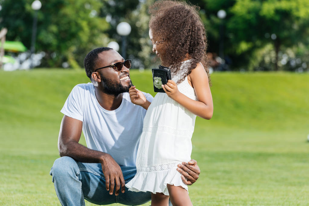 african american daughter standing with police badge and touching father beard in park - Photo, Image