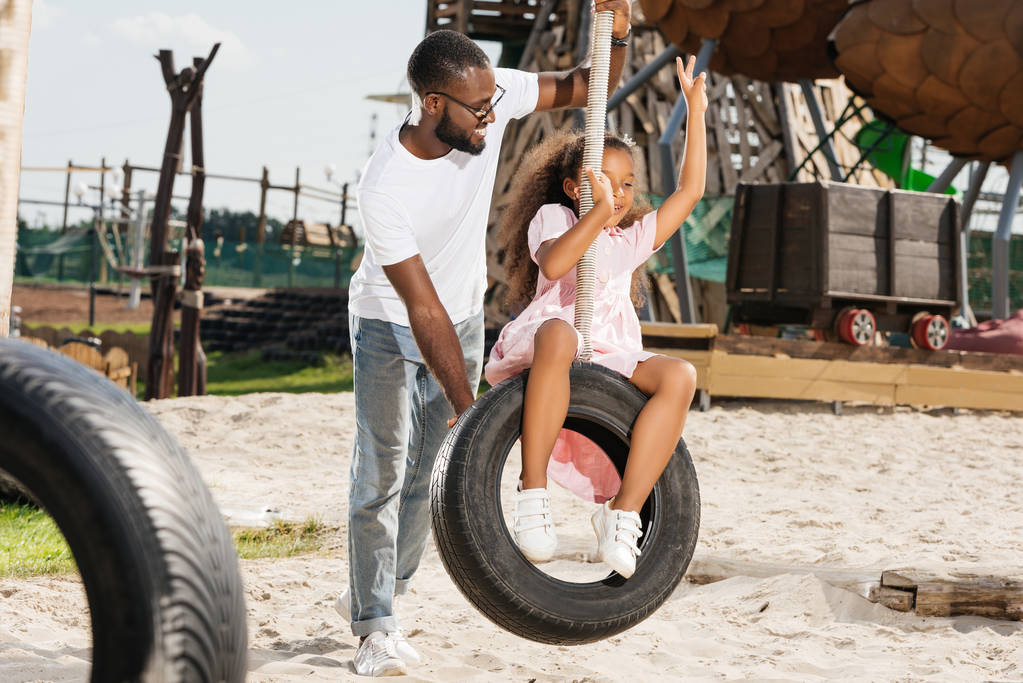 タイヤを 2 本の指を示すアフリカ系アメリカ人の娘が遊園地でスイングします。 - 写真・画像
