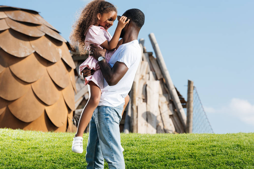 afro-americano pai segurando feliz filha no verde colina no parque de diversões
 - Foto, Imagem