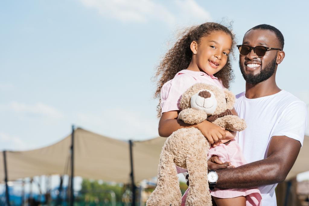 усміхнений афроамериканський батько тримає дочку і вони дивляться на камеру
 - Фото, зображення