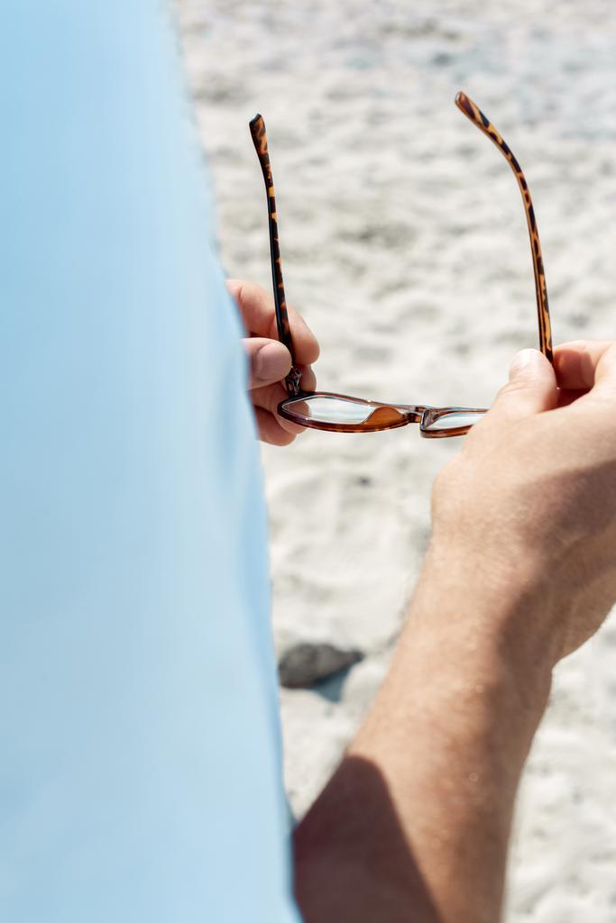 oříznutý snímek člověka drží brýle v rukou na písečné pláži - Fotografie, Obrázek