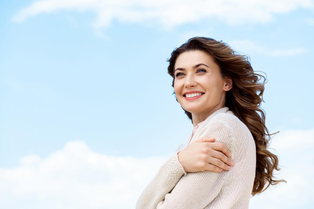вид сбоку улыбающейся красивой женщины на фоне голубого облачного неба
 - Фото, изображение