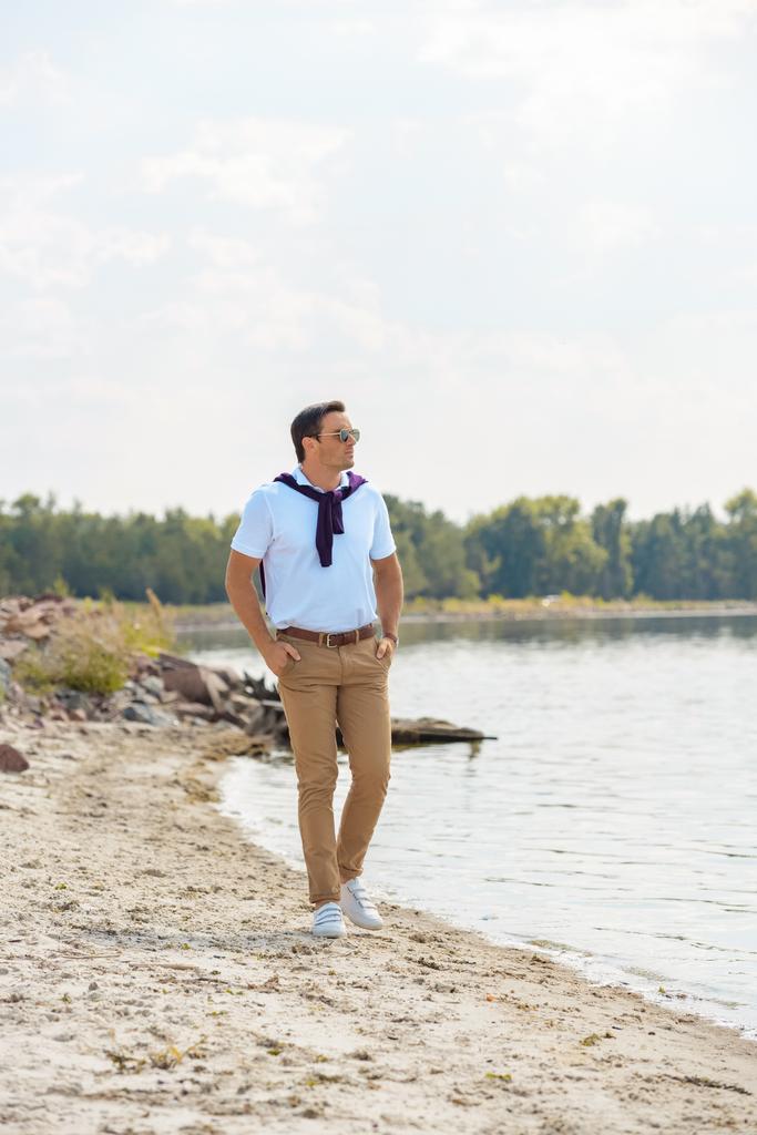 hombre con estilo en gafas de sol caminando solo en la orilla del río arenoso
  - Foto, imagen
