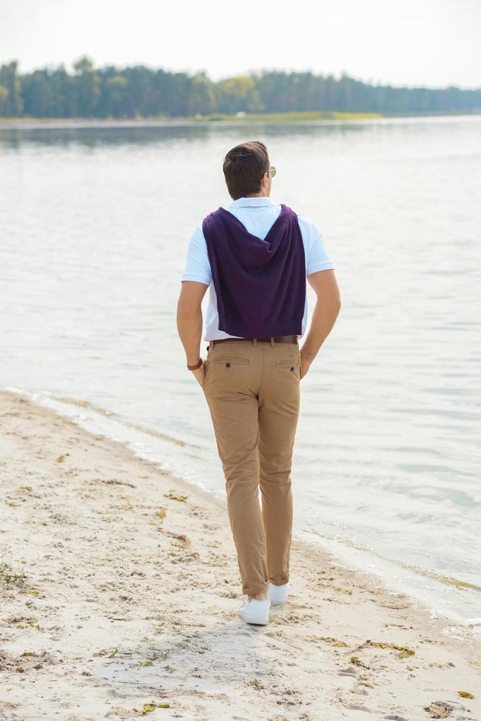 back view of stylish man walking alone on sandy riverbank  - Photo, Image