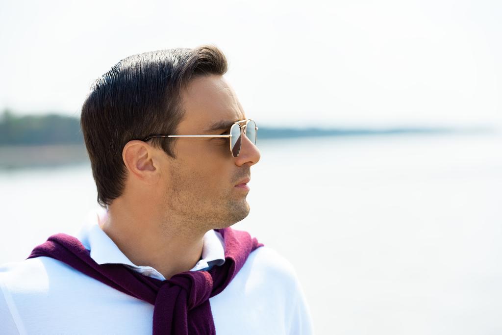 side view of handsome man in sunglasses looking away with river on background - Photo, Image