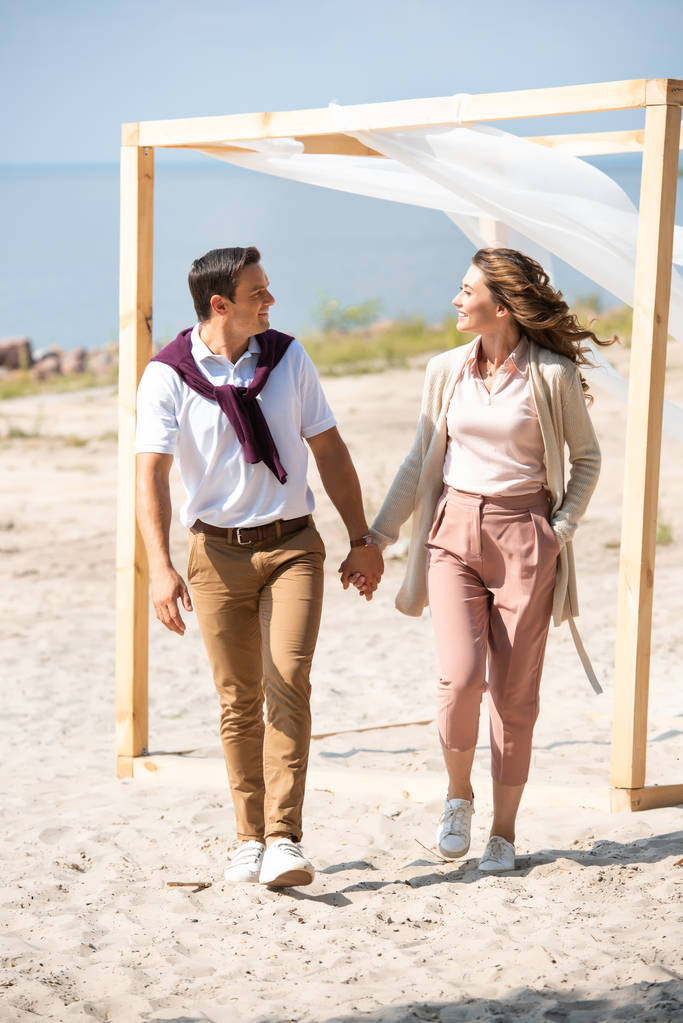 щаслива пара тримає руки під час прогулянки на піщаному пляжі
 - Фото, зображення