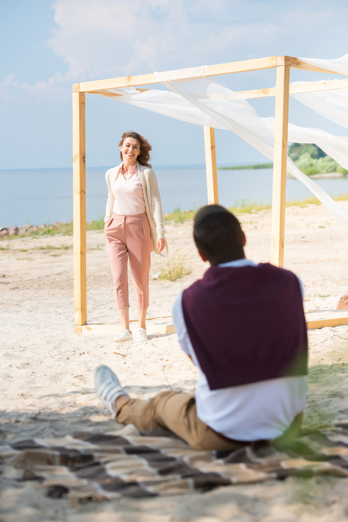 Selektywny fokus człowieka na koc ogląda uśmiechający się żona spaceru na plaży - Zdjęcie, obraz