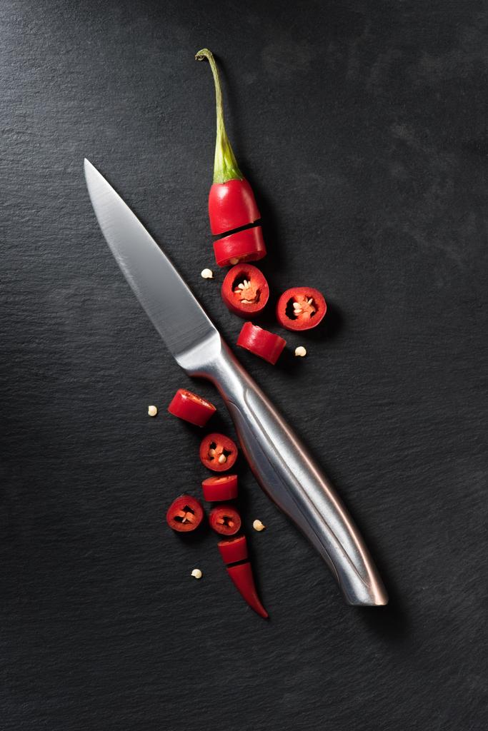 αυξημένη προβολή της κομμένα κόκκινη πιπεριά τσίλι ώριμα και μαχαίρι σε μαύρη επιφάνεια - Φωτογραφία, εικόνα