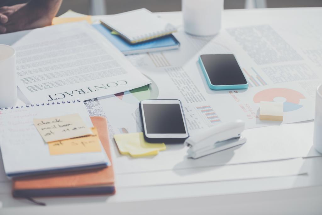 smartphones com contrato e notebooks com grampeador na mesa no escritório moderno, estabelecimento de negócios
 - Foto, Imagem