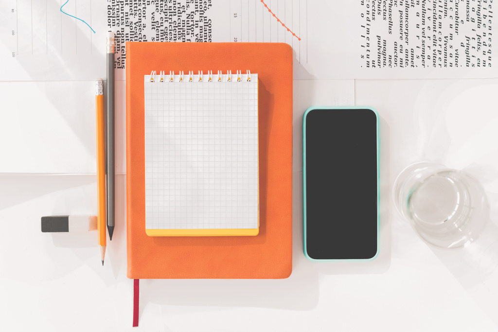 Bovenaanzicht van smartphone met leeg scherm, notebooks en potloden op werkplek - Foto, afbeelding