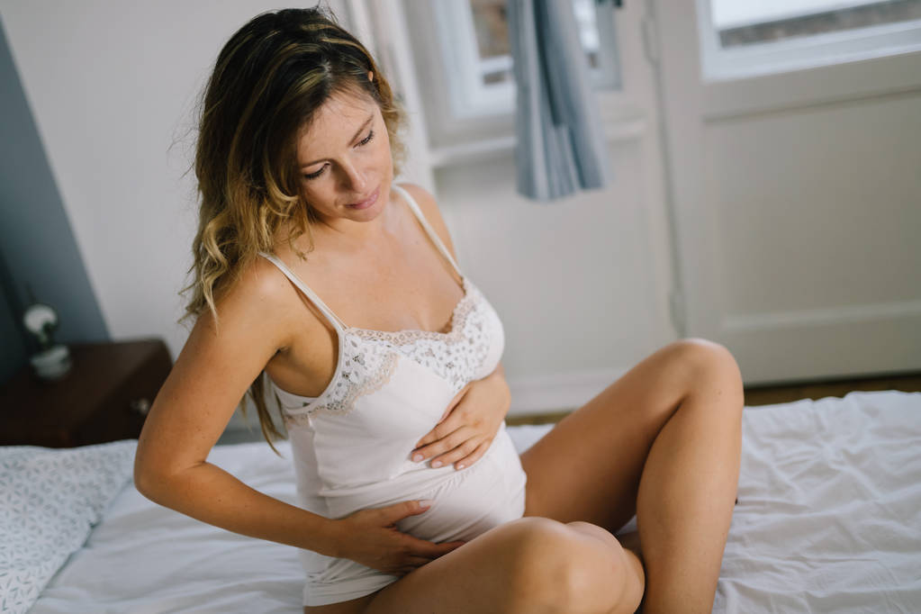 Portret van aantrekkelijke jonge zwangere vrouw zittend op bed - Foto, afbeelding