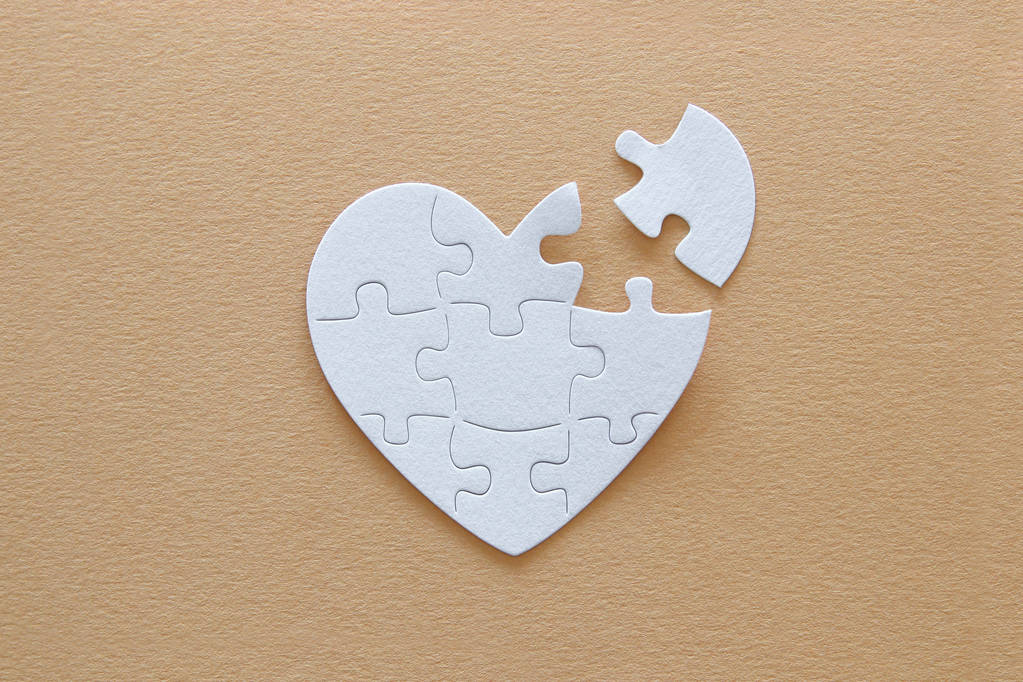 Top view image of paper white heart puzzle with missing piece over brown pastel background. Health care, donate, world heart day and world health day concept - Photo, Image