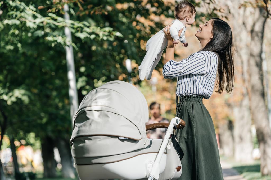 szczęśliwą matką dziecka gospodarstwa w pobliżu wózek w parku  - Zdjęcie, obraz