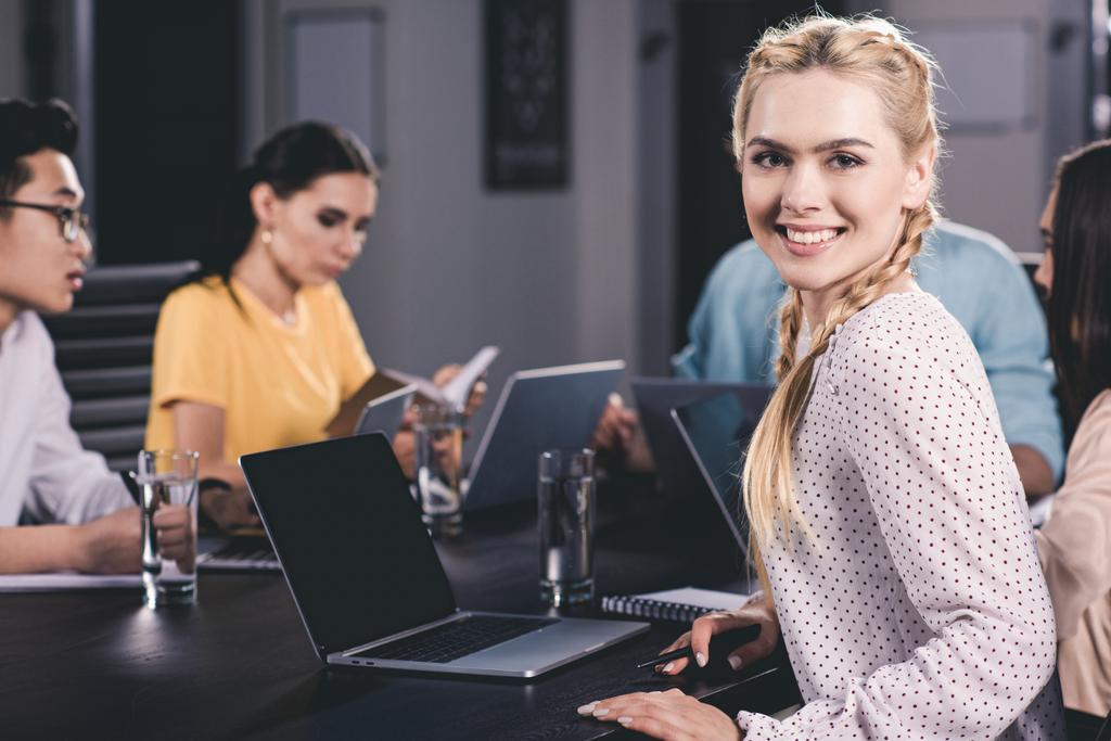 улыбающаяся молодая деловая женщина смотрит в камеру, в то время как ее коллеги работают в современном офисе
  - Фото, изображение