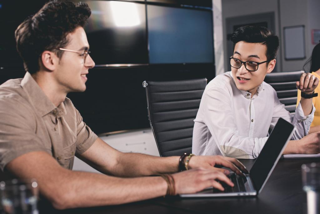 joven asiático hombre de negocios hablando con colega mientras él usando portátil en moderno oficina
  - Foto, imagen