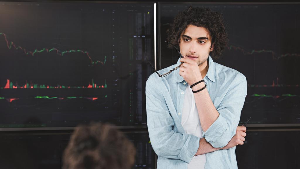 fiatal üzletember, a modern irodában grafikus tábla előtt a kezében áll szemüveg  - Fotó, kép